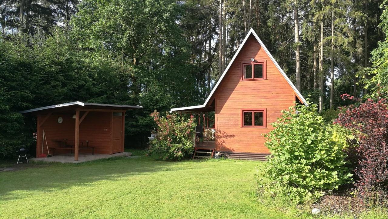Dřevěná chata č. 1 ve tvaru áčka mezi vysokými smrky